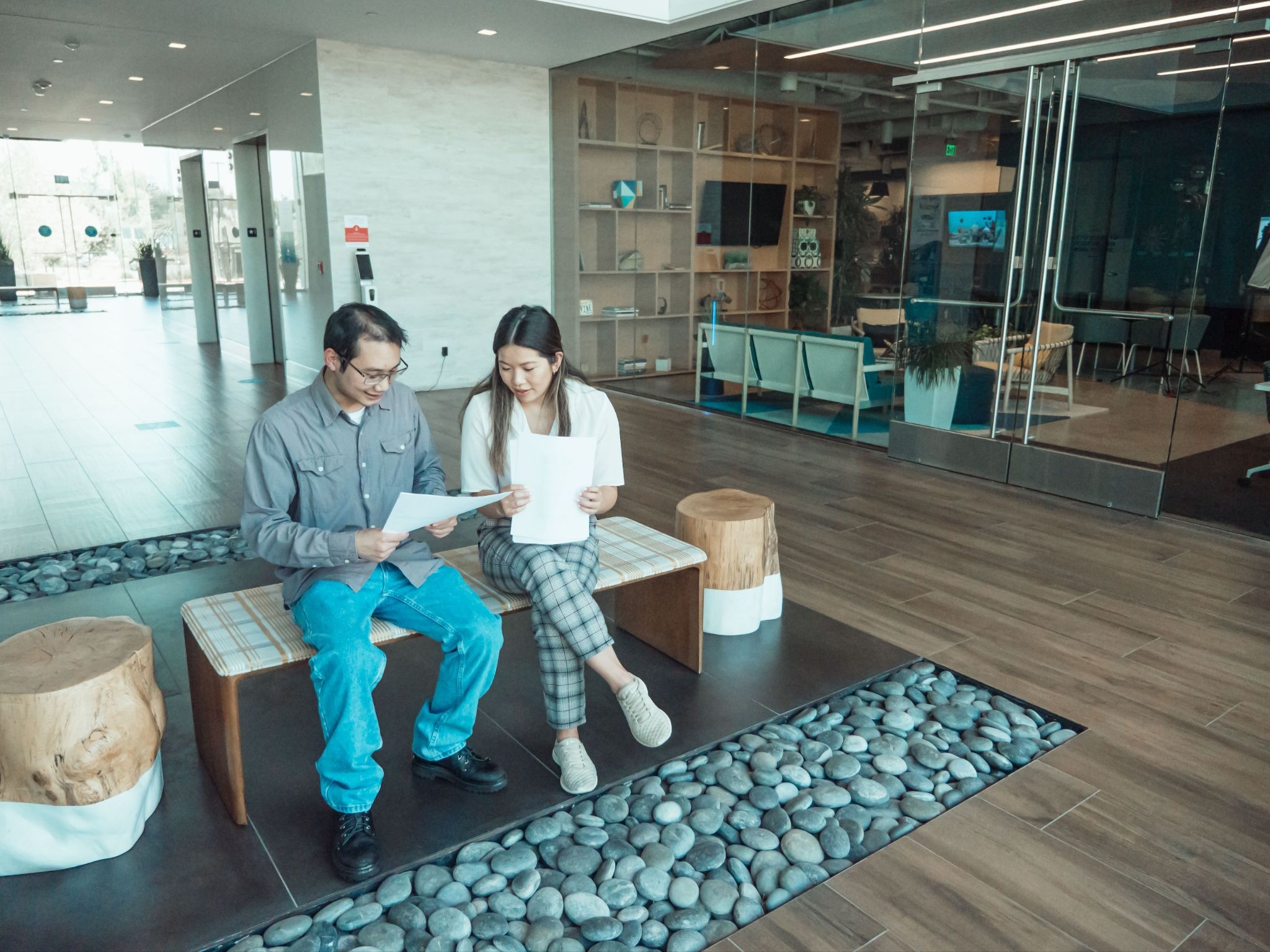 Picture of a man and woman sitting on a bench in a modern office lobby looking at documents