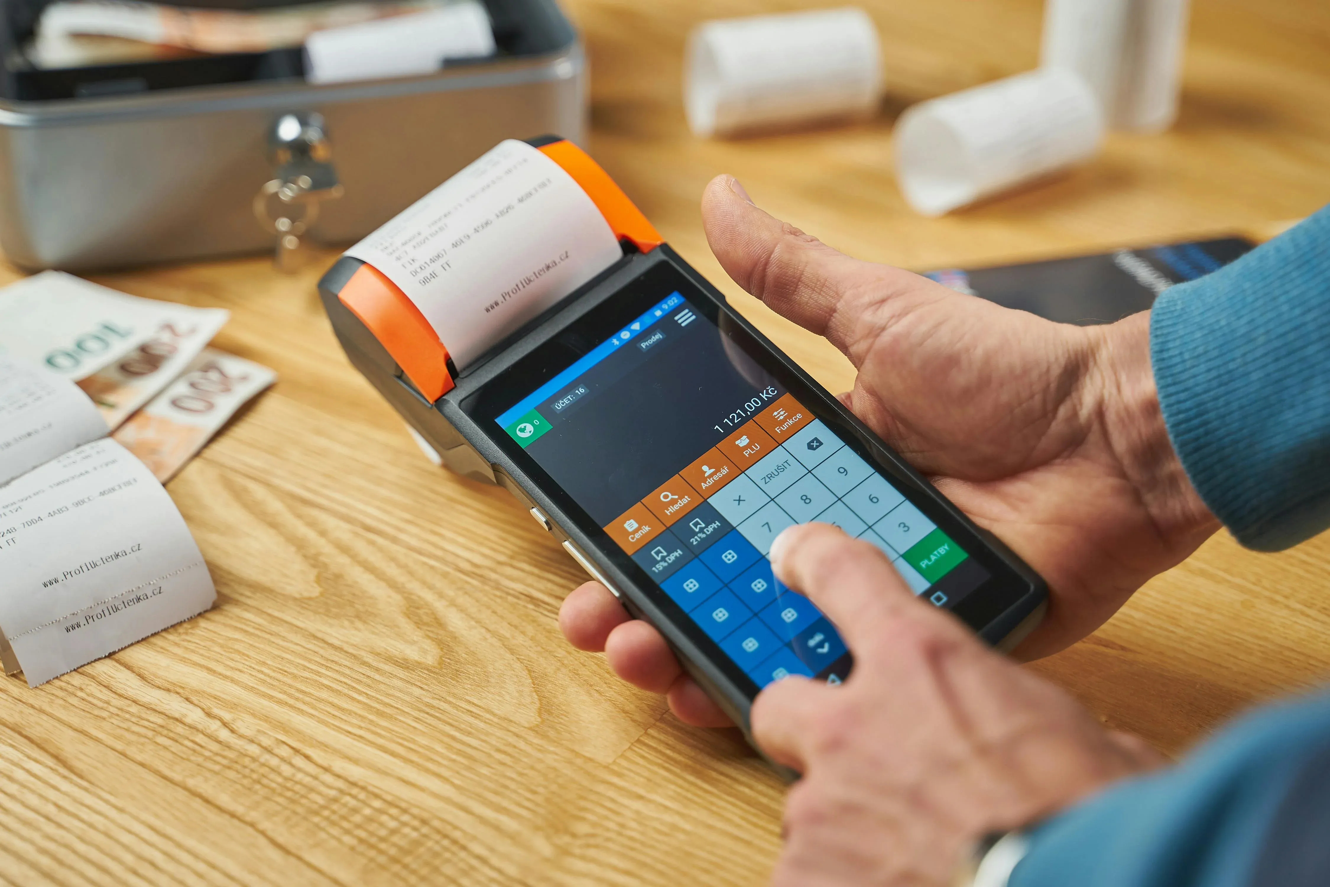 Picture of a person typing on a handheld point of sale device printing a receipt next to cash